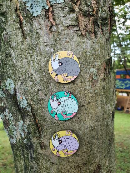 Opossum enamel pins on a tree.