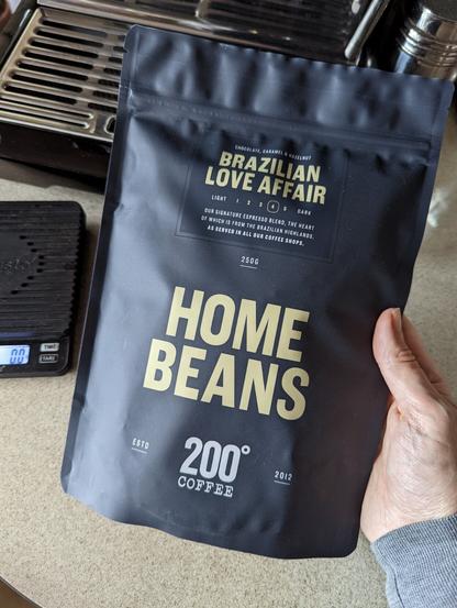 A black bag lettered in gold reads "Brazilian Love Affair" "Home Beans" "200° Coffee"