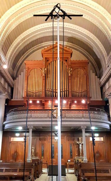 Large church organ pipes viewed from the ground behind a tall microphone stand.