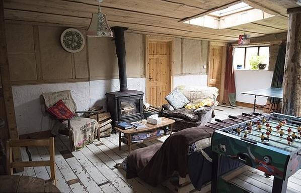 Inside the main space of the Happy Pig.  A wood burning stove, chairs, sofas, table football and table tennis visible inside the wood/cob structure.