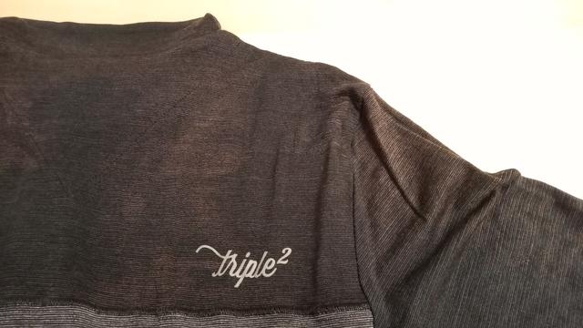 Ein dunkelgraues Fahrradtrikot mit einer kleinen Aufschrift "Triple2". Es sind leicht ins Bräunliche gehenende Verfärbungen, besonders im Nacken- und Schulterbereich, zu sehen.