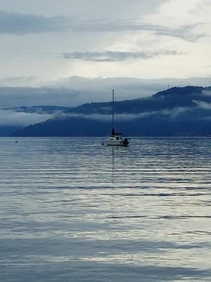 View of a boar in middle of ocean bay, with mountains & fog in the background.