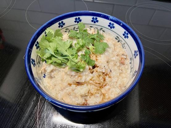 Jook/congee served in a blue and white ceramic bowl, dressed with cilantro and green onion