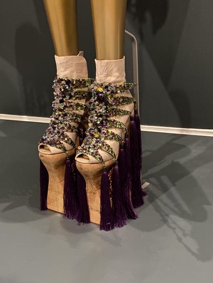 High heel, beaded booties, on precariously high platforms, nearly hidden by purple tassels encircling the base of the shoe.