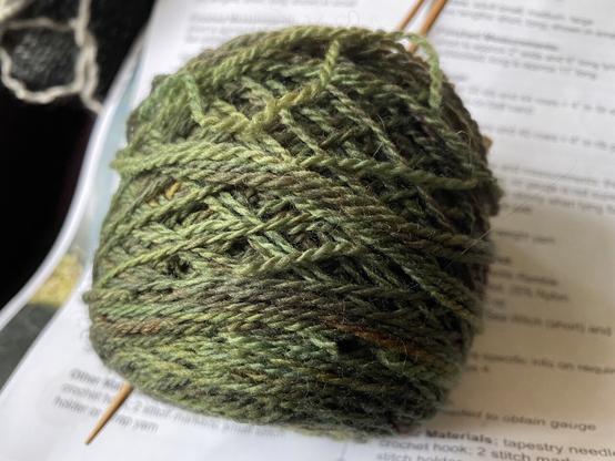 Variegated green ball of knitting yarn with holes indicating carpet beetle feeding and burrowing.