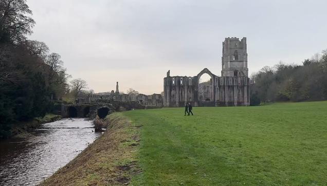 Screenshot of Fountains Abbey via a LIVE tour given by Evelyn Edwards and the Castle Crew pic4 a man walking in the grass next to a stream