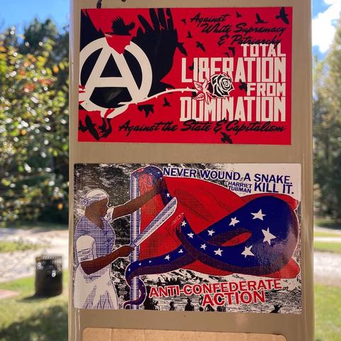 Two stickers in red, black, and blue colors with one focused on “Total Liberation from Domination” and “Anti-Confederate Action”