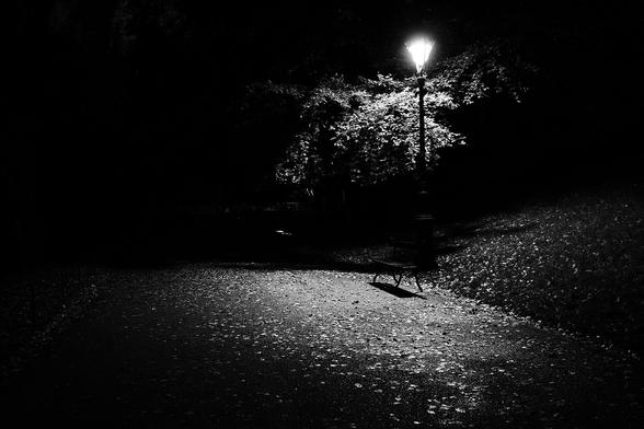 Parc des Buttes Chaumont à Paris, un banc sur la promenade autour du "lac" est éclairé par le lampadaire situé à côté.