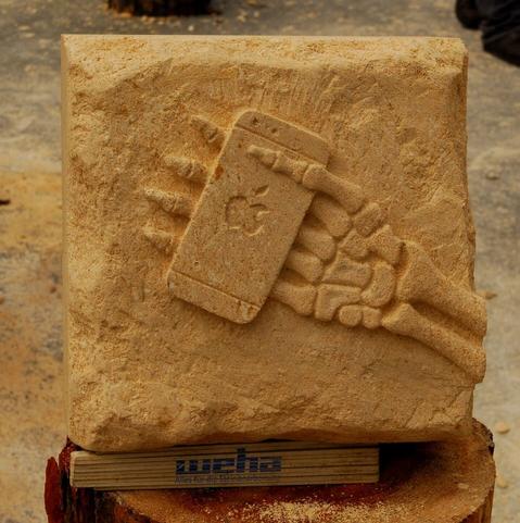 Carved stone block showing a skeletal hand holding an iPhone