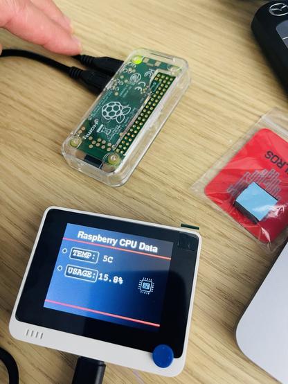 Electronics project. Two fingers holding a Raspberry Pi connected to a separate small screen. The screen shows some sample data emitted by the Raspberry Pi.