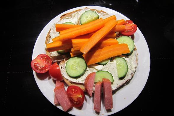 Zwei mit Frischkäse beschmierte Brote, belegt mit Gurken, 2 Tomaten, Karotten, eine dicke Scheibe Wurst.