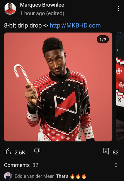 Pictured — Marques Brownlee wearing the latest sweater from his online swag shop. It's a black swear, with pixelated design features which prominently features pixelated snow flakes, shoulder pauldrons and his brand's logo on the front. It gives hockey jersey vibes. 5/5.