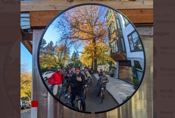 A group of people on bicycles on a city street. Their image is taken from the reflection in a large round mirror.