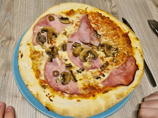 Man sieht eine Pizza mit Schinken und Pilzen und viel Rand