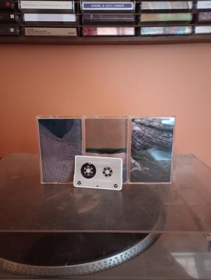 Three cassette tapes from Dinzu Artefacts with sticker in front on top of record player