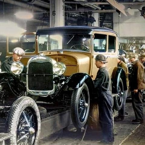 Colourized photo of workmen assembling a Ford Model A sedan on an assembly line.