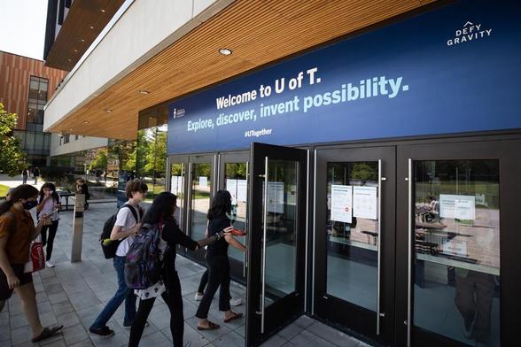 Students walk into a campus building for class. A sign reads “Welcome to U of T. Explore, discover, invent possibility.”