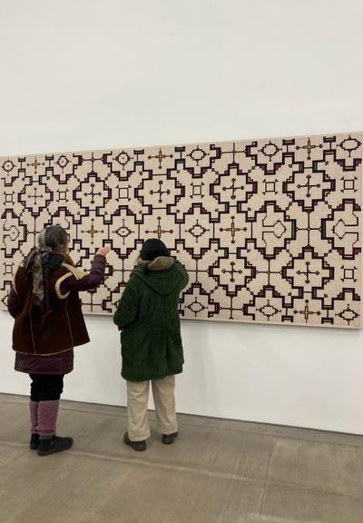 Two people facing a large kené artwork
