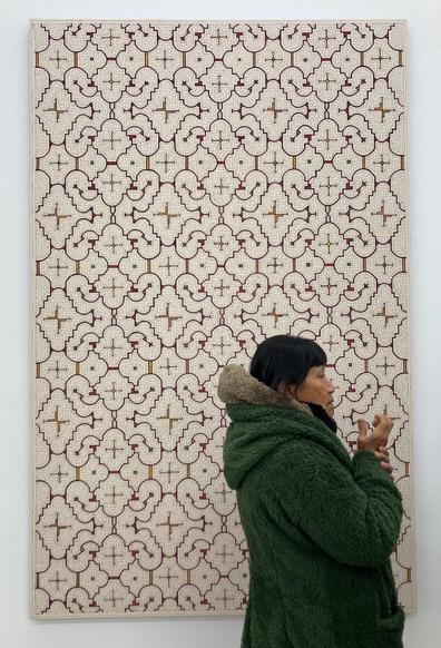 An indigenous-presenting woman with black hair, in profile, with a kené artwork behind her