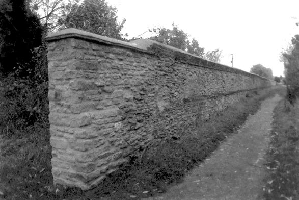 A black and white film photograph of the end of a long ancient stone wall