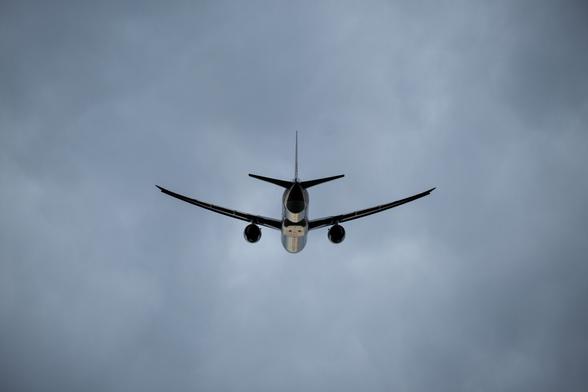 an airliner taking off in the evening, with clouds above, and the sunlight reflecting off its belly.