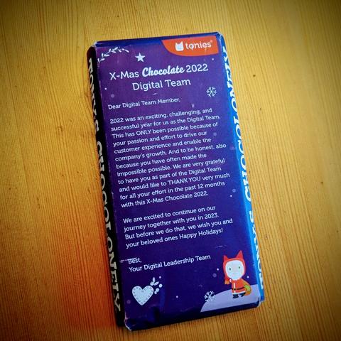 A fair trade chocolate (180g) with a Tonies packaging with a Tonie logo on top. On the front it is written: "

X-Mas Chocolate 2022 Digital Team

Dear Digital Team Member,

2022 was an exciting, challenging, and successful year for us as the Digital Team. This has ONLY been possible because of your passion and effort to drive our customer experience and enable the company's growth. And to be honest, also because you have often made the impossible possible. We are very grateful to have you as part of the Digital Team and would like to THANK YOU very much for all your effort in the past 12 months with this X-Mas Chocolate 2022.

We are excited to continue on our journey together with you in 2023. But before we do that, we wish you and your beloved ones Happy Holidays!

Best,

Your Digital Leadership Team"

A small drawn heart, two snowflakes and a Tonie dressed as Santa Claus are underneath.