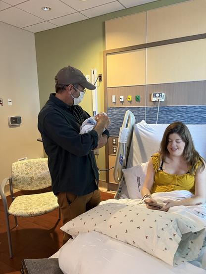 Me holding my grandson next to my daughter still in her hospital bed.