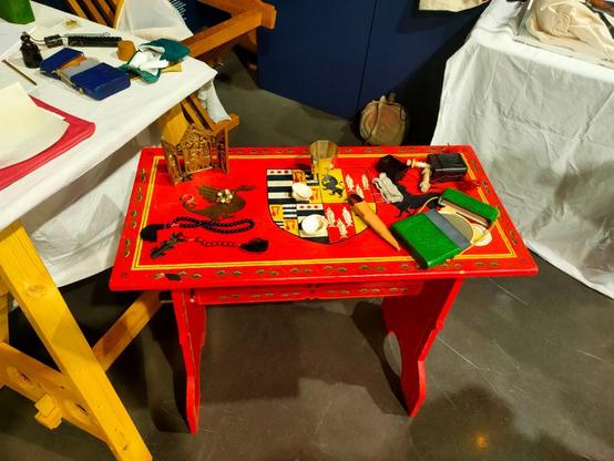 Sur une table rouge sont disposés différents objets : un autel portatif, un miroir et un nécessaire à couture dans leurs étui, un verre, deux coquilles Saint-Jacques, une paire de ciseaux.