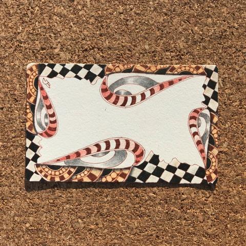 A white Phi Zentangle tile with black and brown ink. Shade with graphite and red pastel chalk pencils