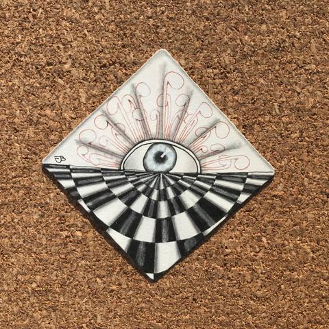A white Zentangle tile with a check board pattern drawn in black in one half, and a large sun rushing over the other half. The centre of the sun has a eyeball drawn in blue. The tile is shaded in graphite