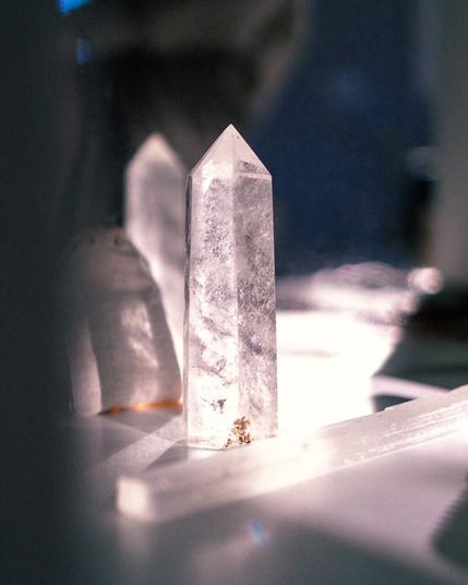 A clear quartz crystal tower next to a long, rectangular clear crystal. The background is dark, but the crystals are illuminated in sunlight.