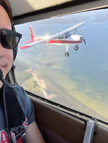 View out the window of a small aeroplane looking at a Cessna 180 aeroplane in formation