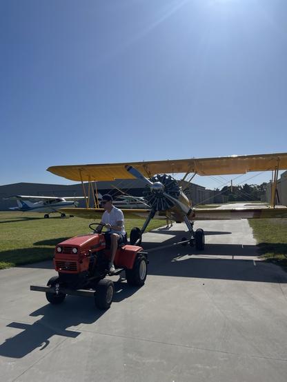 A small tractor towing a Boeing Stearman biplane under a clear blue sky