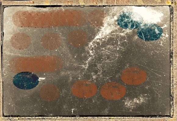 The outer frame of this composition is aged brown with edges like an old snapshot.  The image background is a dull brown monochrome, covered in white scratches & blotches.  There are small green and rusty brown elongated ovals that are stamped  & smeared over parts of the surface. The overall impression is of an old photo of a surface, possibly glass or ice, which has been stained or spotted with paint or ink.