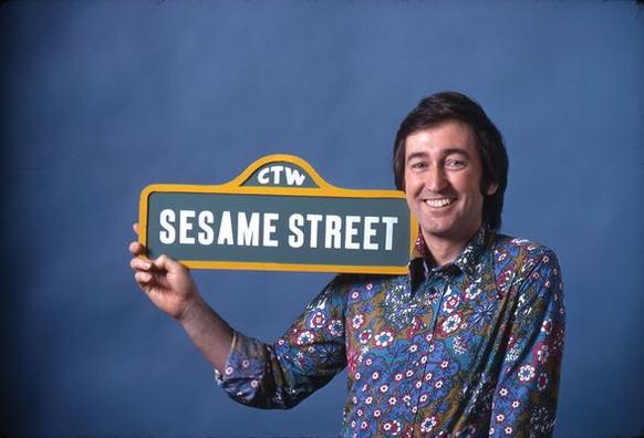 Bob McGrath holding up the Sesame Street sign.