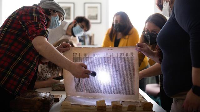 Researchers crowd around a book that they examine with a flashlight
