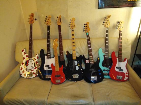Row of 8 bass guitars sitting on the couch.