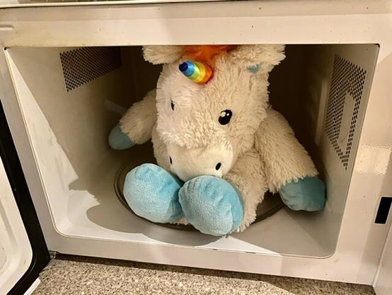 Open microwave entirely filled by a white stuffed unicorn (containing lavender). The rainbow horn sticks out from the front and there’s no dignified way for the unicorn to fit. Though I don’t suppose it would look dignified even in a bigger microwave.