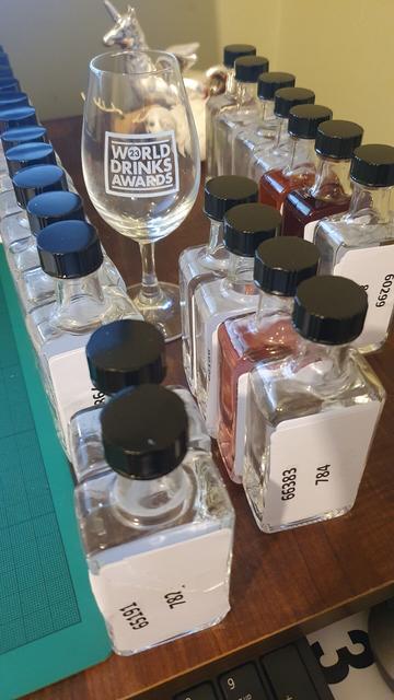 Several rows of small gin sample bottles alongside a 'world drinks awards' branded tasting glass.