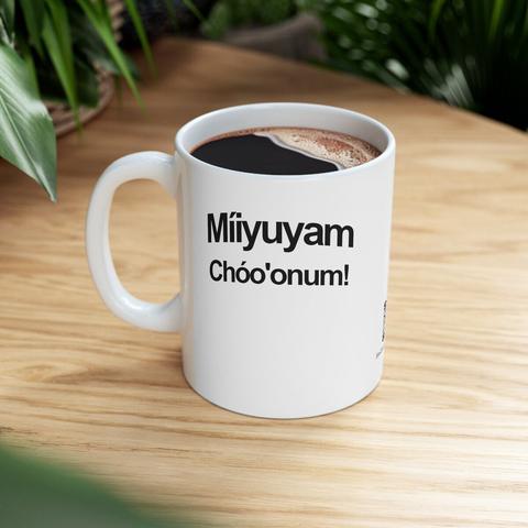 White coffee mug on a blurred neutral wood desk. 80’s retro black font in an arc. It reads: “Míiyuyam Chóo'onum!” (Hello Everyone!)