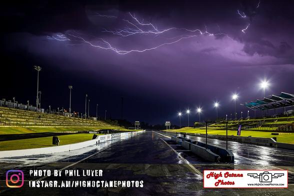 Photo of a drag strip at night as lightning bolts shoot through the night sky.