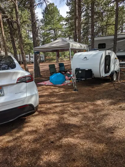 Small teardrop camper at campground, Tesla model Y to the lower left.