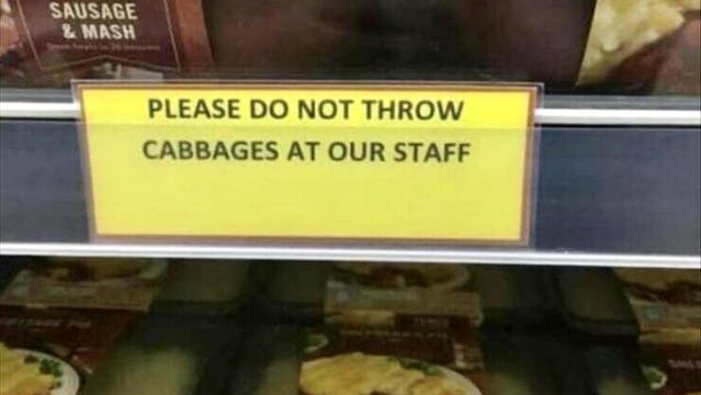 Sign on market shelf reading “Please do not throw cabbages at our staff”