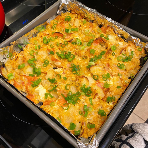 Baked seafood blended with cream cheese on sushi rice in a casserole dish, topped with chives
