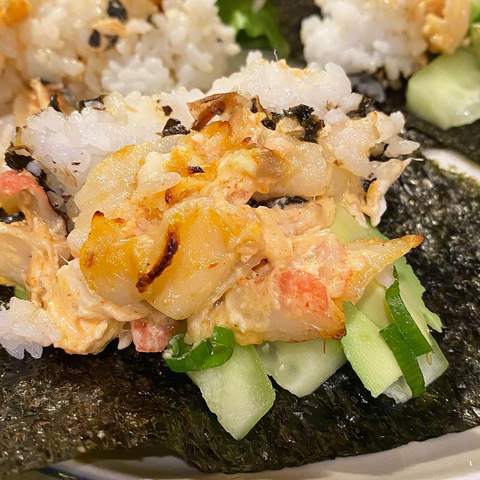 Close up of seafood blend on top of sushi rice, cucumbers, and avocado, sitting on a sheet of nori