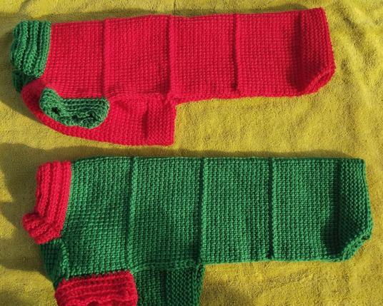 Two dog sweaters, identical in size. One is red with green trim (collar and sleevelets), the other is the opposite color combination (green with red trim on the collar and sleevelets).
