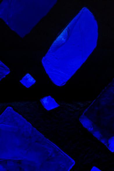 A photograph showing a close up view of sunlight filtered through the oddly-shaped medium-blue, translucent glass chunk “windows” of varying sizes embedded in one of the concrete panels that make up the walls, floor to ceiling,  of the Great Hall  at the New York Hall of Science, the former science pavilion of the 1964 Worlds Fair.