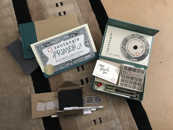 An unpacked parcel of products from Zentangle, which includes their art box, their Primer, some journals, and blank black tiles with white pens