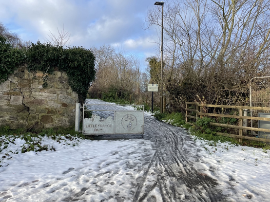 Entrance into park. It says Little France Park on the sign. Ice on path.
