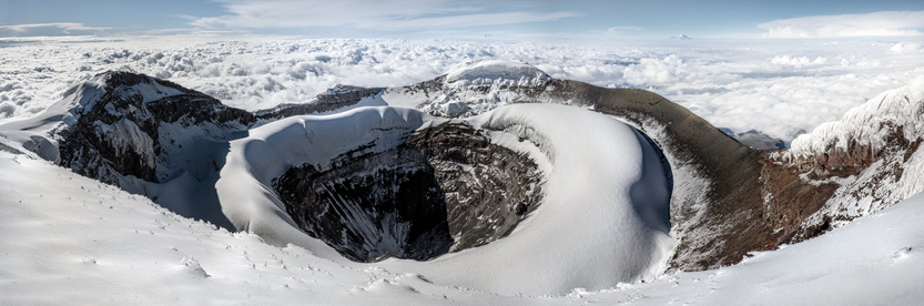 Cotopaxi is an active stratovolcano in Ecuador reaching a height of 5,897 m (19,347 ft). Featured here is the volcanoes cone viewed from the summit rim. In the distance is Chimborazo poking through the clouds.